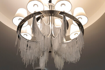 A round chandelier with fabric light shades and a metal case, from which many silver chains of different lengths hang down.