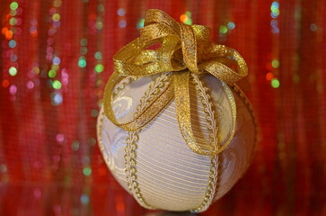 A fancy eggwhite linen Christmas ornament with gold ribbon on a mirror on a shiny red bokeh background