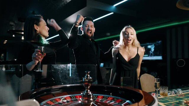 Excited group of bearded man and two beauty woman are winning at casino roulette table