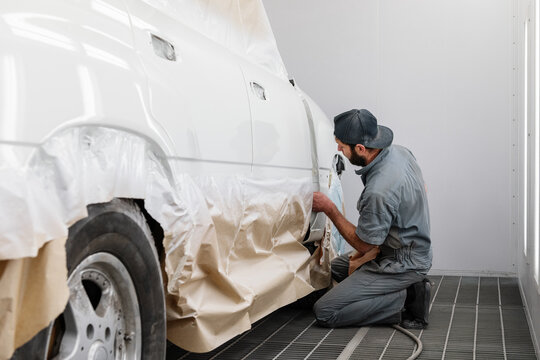 Bearded technician checking paint on car under cover
