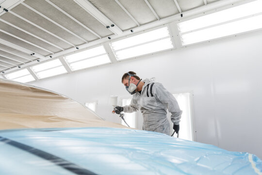 Technician painting car with cover