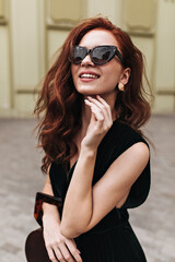 Ginger woman in trendy sunglasses poses outside and smiles