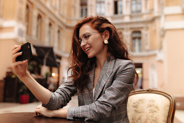 Red haired lady in grey jacket takes selfie in street cafe