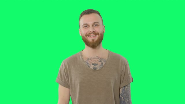 Happy handsome man on chroma key. Positive bearded tattooed hipster is looking to the camera and smiling on green screen background. Isolated portrait for keying