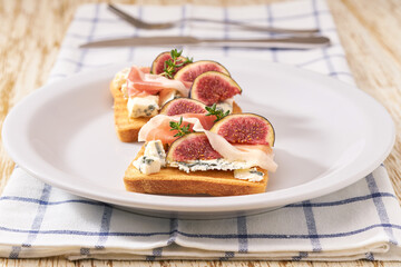Open sandwich with blue cheese, prosciutto and fresh figs on a white ceramic plate.