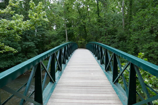 Wooden footpath bridge with metal handrails crossing creek through forest perspective © Adventuring Dave