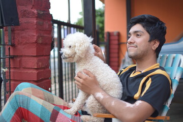 young man sitting stroking a poodle dog