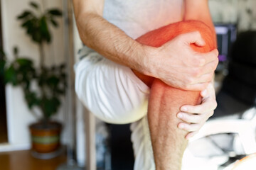 a man holds his knee in pain against the background of the room