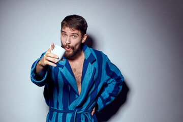 man in a blue robe with a white cup in his hand on a light background gesturing with his hands cropped view