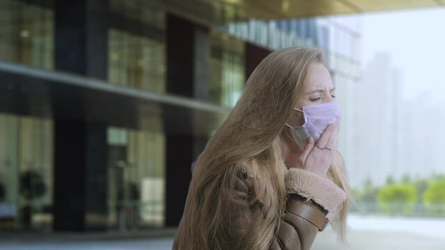 Woman wearing face mask because of Air pollution or virus epidemic on the street background. Portrait of infected woman coughing. A sore throat