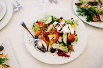 Greek salad in a white plate at the background of the table. Close up. Top view.