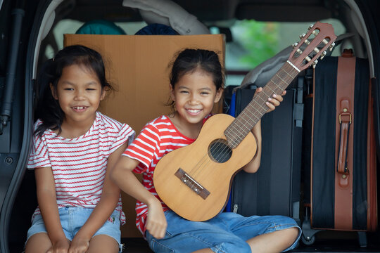 Happy Asian Child Girl Playing Guitar And Singing A Song With Her Sister In A Car Trunk In Family Trip.