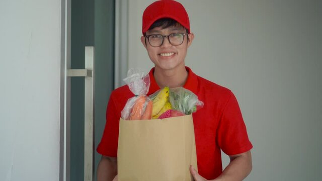 close up young postal worker ( red uniform ) smiling with carrying box and stand in front of house for waiting to send  order to customer for business and e-commerce lifestyle concept