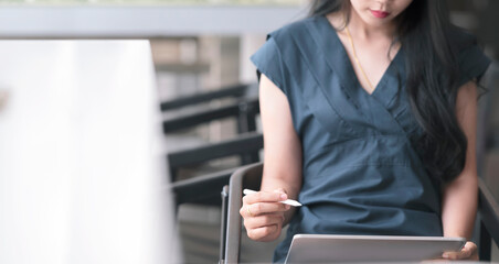 Cropped photo hands of young female designer holding stylus pen and working with tablet while sitting at her office, copy space.