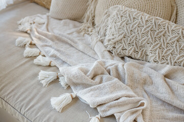 White knit blanket lying on the corner sofa in the living room, macrame pillows around