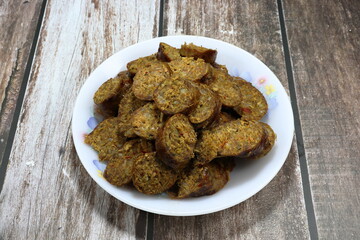 Pile of sliced spicy pork sausage marinated with spices herbal vegetable in Thai style on the plate. Famous appetizer menu in local Asia restaurant. 