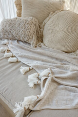 Angled closeup view of white macrame  pillow and a knitted blanket lie  on a beige sofa with soft focus