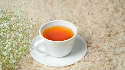 White cup with tea placed on a cream carpet. Decorated with white flowers in the corner. 