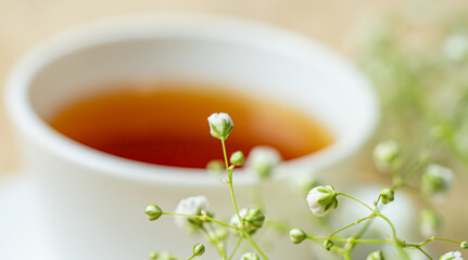 White cup with tea placed on a cream carpet. Decorated with white flowers in the corner. 