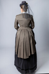 A middle-aged woman dressed in a Victorian costume and holding a fob watch and a walking cane