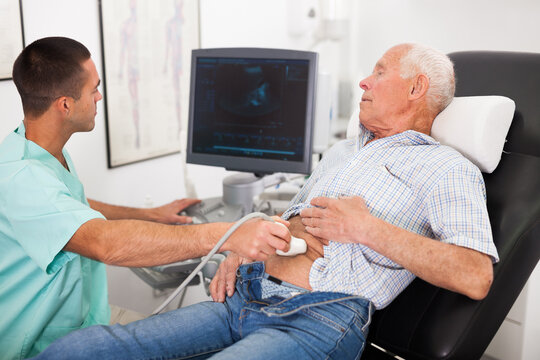 Young male doctor using ultrasound scan doing abdominal diagnostic to senior male patient in modern clinic