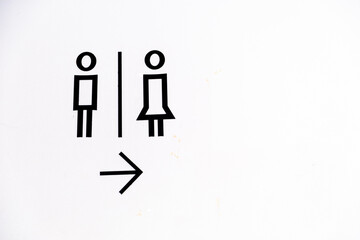 Fototapeta premium Toilet sign with simple black icon of male and female with arrow pointing to the right against white concrete wall. 