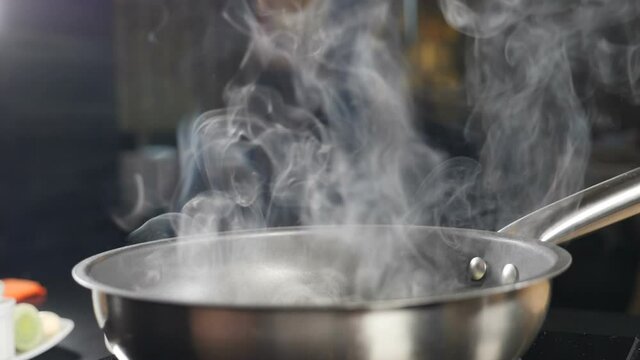 White smoke in slow motion rising above hot frying pan on black background. Cooking in restaurant. Delicious risotto being cooked in restaurant kitchen. Full hd