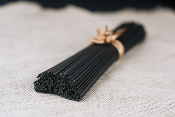 Raw black homemade spaghetti bunch with ribbon on canvas rag. Dry black noodles macaroni bundle.