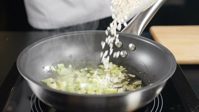 Cooking delicious risotto in frying pan. Chef pouring Rice in slow motion. dry basmati rice falling down. Italian cuisine. Full hd