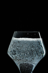 Mineral water is poured into a glass. Black background.