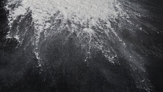 Flour is falling on the black table in slow motion. Someone throwing flour on a dark background. Slow motion of falling white flour on the black background. 