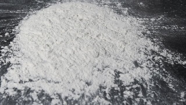 Flour is falling on the black table in slow motion. Someone throwing flour on a dark background. Slow motion of falling white flour on the black background. 