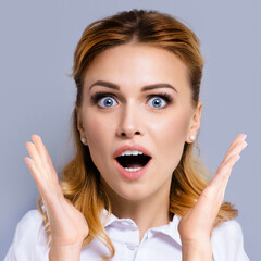 Excited surprised, shocked or very happy amazed businesswoman with wide open mouth and eyes, raised up hands. Face portrait studio image, square composition.