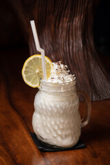 Homemade tasty milk shake cocktail on a jar, vanilla milkshake banana smoothie, whip cream , ice cream, white, lemon on dark wooden table, chocolate cinnamon, vertical. 