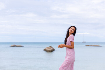 Young romantic girl with long dark hair in dress on the beach, smiling and laughing, having a nice time alone.  