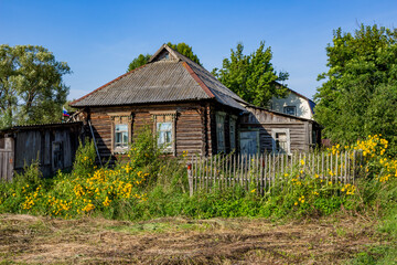 Fototapeta na wymiar View of the old wooden village house in the Russian village. Overgrown plot with a picket fence 