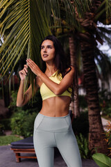 Fototapeta na wymiar Outdoor portraif of fit slim sporty tanned pretty caucasian woman in sport yellow top and leggings on tropical background, sunny day, bright light. 
