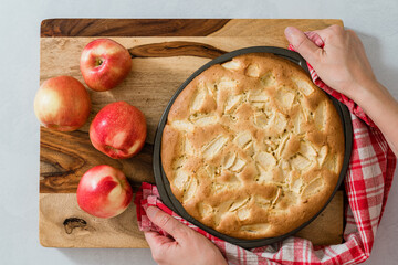 Fresh baked Apple cake, soft and moist, with sliced apples, close up on wooden board. Flat lay, woman hands