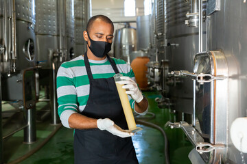 Fototapeta na wymiar Man worker of winery in protective mask checking wine production process at fermentation tank