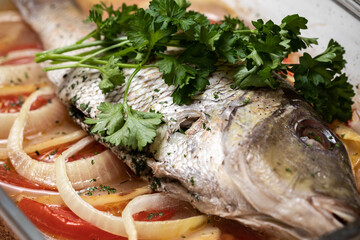 Marinated grilled whole sea baked fish with tomato, onion, parley, lemon, sauteed vegetables. Food on a white plate. 