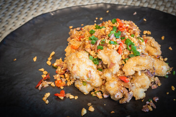 Deep fried sea bass with chili and salt in a black plate, served on the dining table. Snapper is a diet that helps you lose weight and improve your brain.