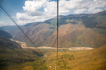 Wonderful panoramic view into Chicamocha Canyon with river bed, white clouds and blue sky with cables of aerial cable car, Columbia