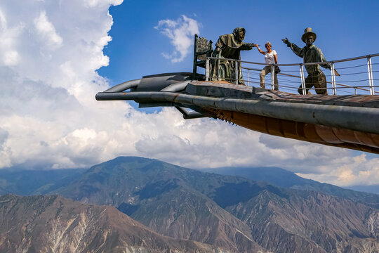 Panoramic view of a person on a part of Monument of the Virgin Mary soaring into the sky against blue sky and white clouds, Chicamocha Canyon, Colombia