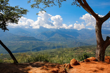 Panoramic view from Barichara, Colombia over green landscape to mountains with blue sky and white clouds along the mountain ridge, trees and red earth in foreground