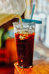Iced coffee in a tall glass on a wood table with cream  poured over