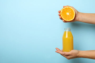 Female hands hold orange and bottle of juice on blue background