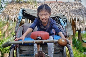 A cute young Asian girl riding a vintage tricycle with passenger seat in the back, having fun and...