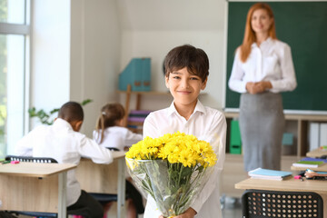 Little schoolboy with bouquet for his teacher in classroom