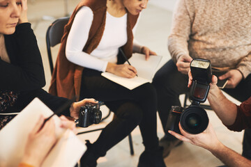 Small group of attendees sitting in photography studio and listening to their tutor who is talking about camera parts.