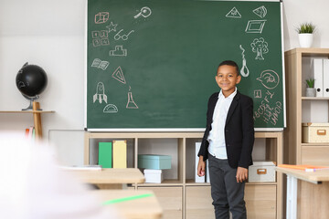 Cute little African-American schoolboy near blackboard in classroom